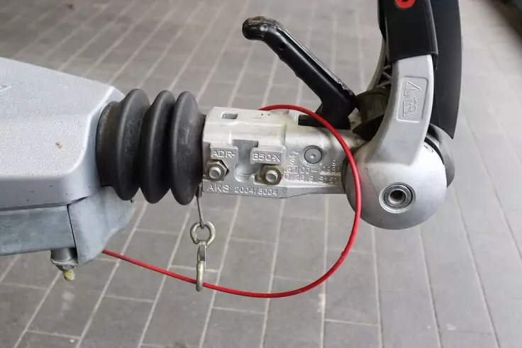 Nahe Aufnahme einer Metallkupplung mit rotem Kabel, Schlüssel an einem Ring, schwarzem Hebel, Gummimanschette und grauem Fliesenboden