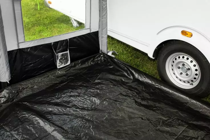 Schwarzer Kunststoffboden, offenes Seitenfenster mit sichtbar grünem Gras, rechts weißes Rad eines Fahrzeugs