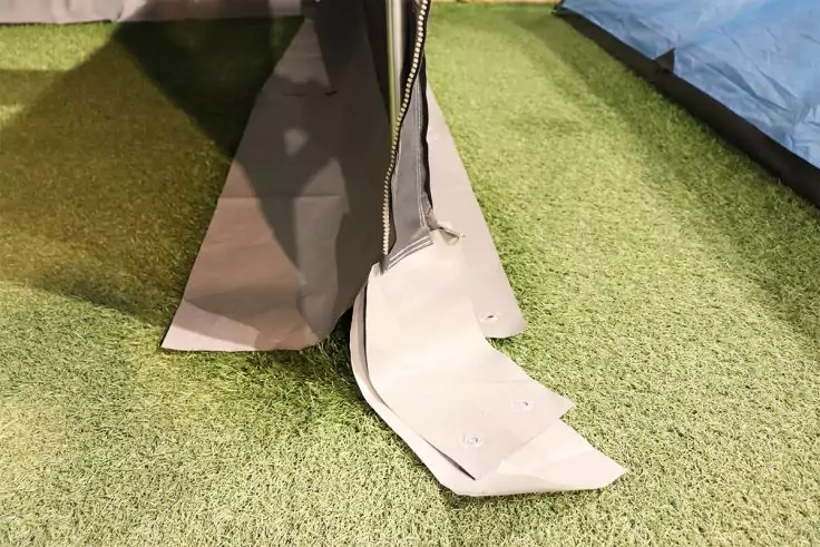 Beigefarbener Stoff mit offenem Reißverschluss liegt auf grünem Rasen neben blauem Stoff