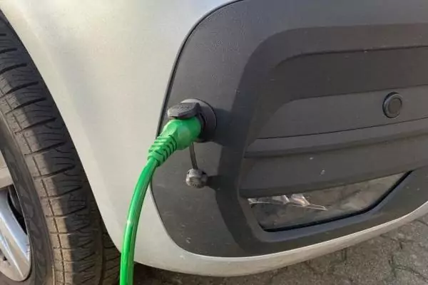 Silbernes Auto, grünes Ladekabel steckt in der Ladebuchse neben dem vorderen Reifen
