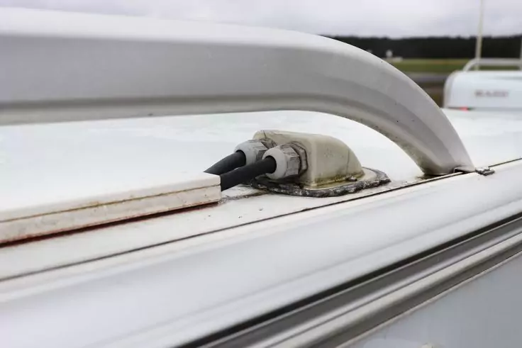 Nahaufnahme einer weißen Dachreling auf einem weißen Dach mit einer Kabeldurchführung, zwei schwarzen Kabeln und Dichtmasse