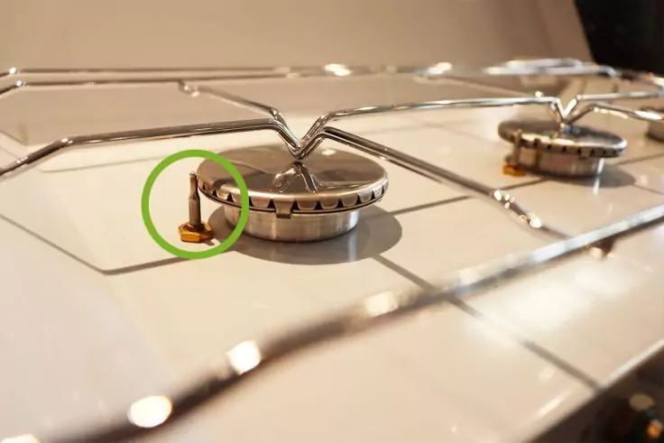 Kochfeld mit zwei Brennern und Metallgitter; links neben dem vorderen Brenner ein kleines braunes Bauteil, grün eingekreist