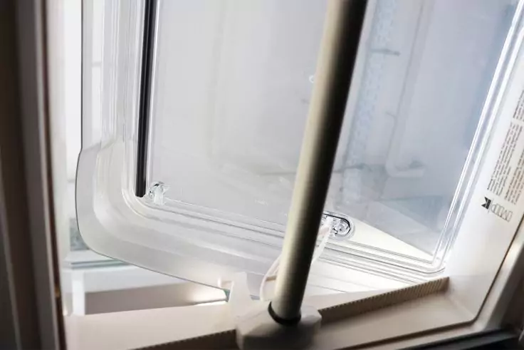 Kippfenster aus weißem Kunststoff, obere Scheibe schräg gekippt, senkrechte Metallstütze, sichtbare Dichtung und Etikett