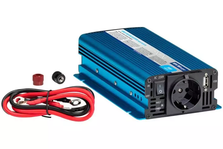 Blaues rechteckiges Metallgehäuse mit eingebauter Steckdose, USB‑Anschluss und Schaltern; daneben rote und schwarze Anschlusskabel mit Ringösen und zwei kleinen Isolierkappen