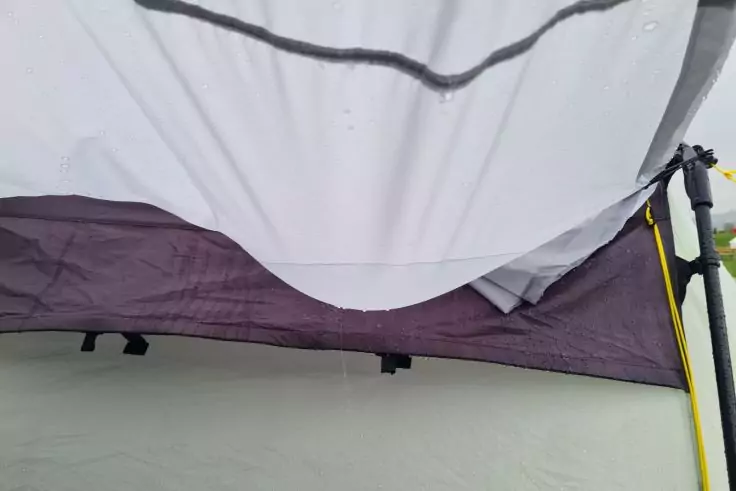 Weißer Stoff mit dunkler Naht oben, violette Stoffkante darunter, grauer Boden; rechts gelbe Stange mit schwarzem Anschluss und grünem Clip