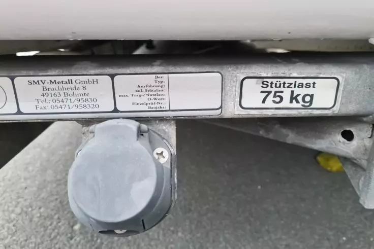 Metallrahmen mit Firmenplakette und Aufkleber 'Stützlast 75 kg', runder grauer Steckanschluss mit Schutzkappe, grauer Asphalt und kleines gelbes Blatt