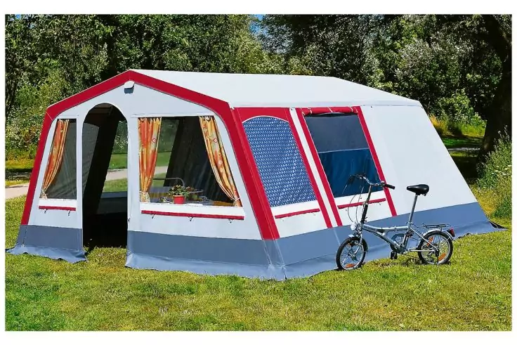 Großes weiß-rotes Zelt mit offenem Eingang und Fenstern mit Vorhängen auf Gras; ein Fahrrad lehnt am Zelt; Bäume im Hintergrund