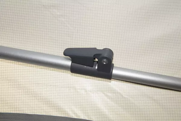 Silberne Metallstange mit schwarzer Kunststoffklemme vor hellem Stoffhintergrund