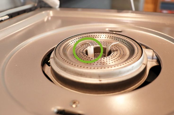 Nahaufnahme eines runden Metallbrenners auf einem Herd mit vielen kleinen Öffnungen und einer weißen, stiftförmigen Keramikeinlage in der Mitte