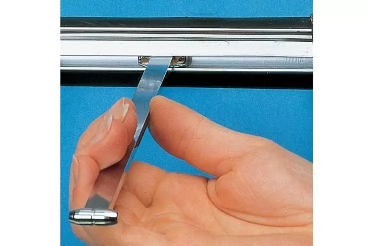 Hand hält Metallhaken an einer Bilderschiene vor blauem Hintergrund