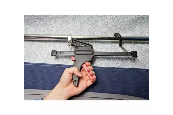 Hand hält ein schwarzes, pistolenförmiges Werkzeug an einer silbernen Metallschiene; darunter blaues Polster, graue Wand im Hintergrund