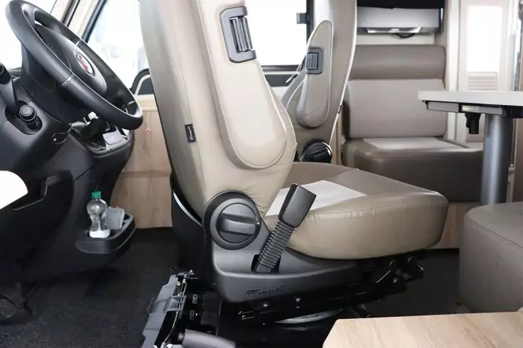 Fahrzeuginnenraum mit beigen Vordersitzen, Lenkrad, Tisch, Sitzbank, Sicherheitsgurt und einer Flasche im Becherhalter