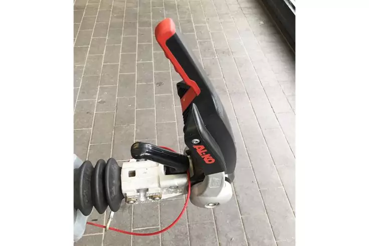 Schwarz-roter Griff mit rotem Kabel an metallischem Mechanismus, schwarzer Faltenbalg, graue Bodenfliesen