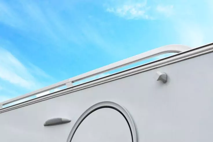 Weiße Seitenwand mit rundem Radkasten, Türgriff, Dachreling und blauem Himmel