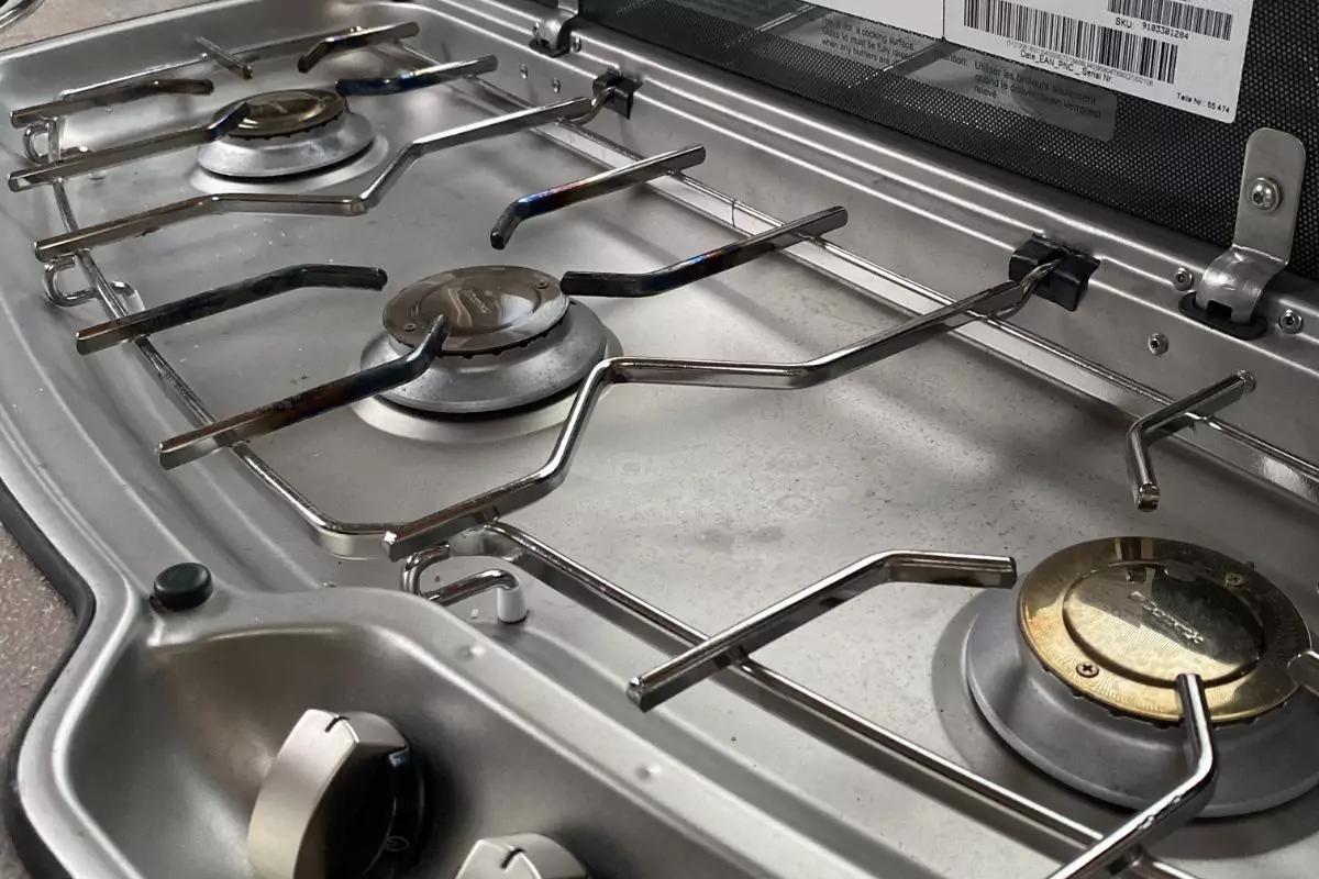 Metall-Kochfeld mit drei sichtbaren Brennern, Metallgitter, einem Drehregler und leichten Flecken