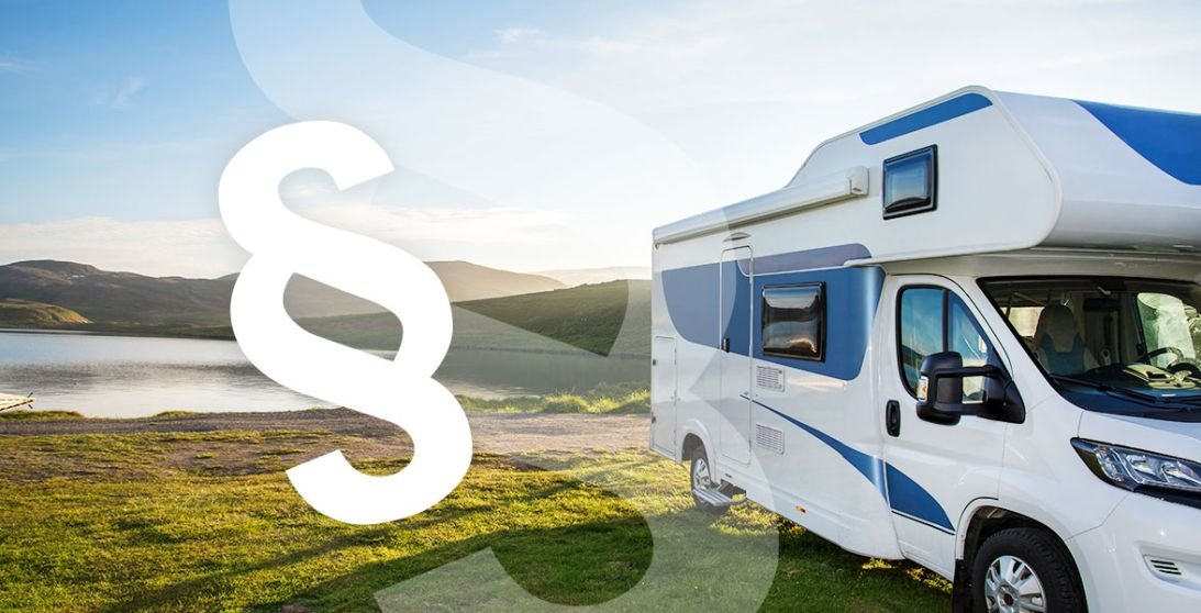 Wei&szlig;es Wohnmobil auf Gras neben einem See, gro&szlig;es wei&szlig;es Paragrafenzeichen im Vordergrund, H&uuml;gel und bew&ouml;lkter Himmel im Hintergrund