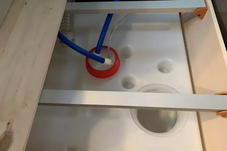 Wei&szlig;er Innenraum mit mehreren runden &Ouml;ffnungen und Vertiefungen; zwei blaue Schl&auml;uche f&uuml;hren durch eine rote runde Einfassung; helle Holzleisten und Holzplatten an den Seiten