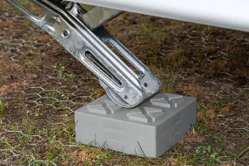 Ausfahrbares Metallst&uuml;tzbein steht auf einem grauen Kunststoffblock auf grasigem Boden