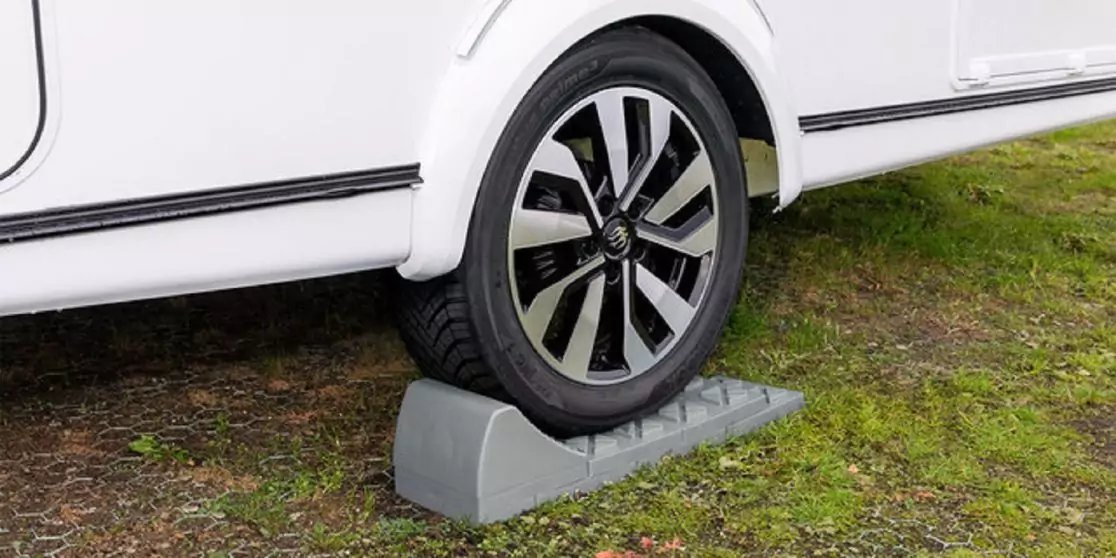 Rad eines wei&szlig;en Fahrzeugs auf einer grauen Auffahrrampe auf Gras und Kies