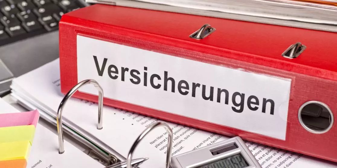 Roter Ordner mit Etikett 'Versicherungen', ge&ouml;ffnete Ringmechanik, lose Papiere, Taschenrechner, Tastatur und Haftnotizen