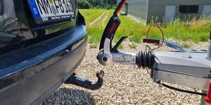 Heck eines schwarzen Autos mit Kugel-Anh&auml;ngerkupplung, an eine Anh&auml;ngerzugvorrichtung gekoppelt; Schotterboden, Gras und Geb&auml;ude im Hintergrund