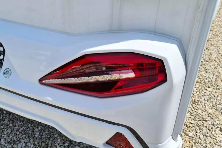 Nahaufnahme eines roten R&uuml;cklichts an der wei&szlig;en Hecksto&szlig;stange eines Autos, darunter Kies