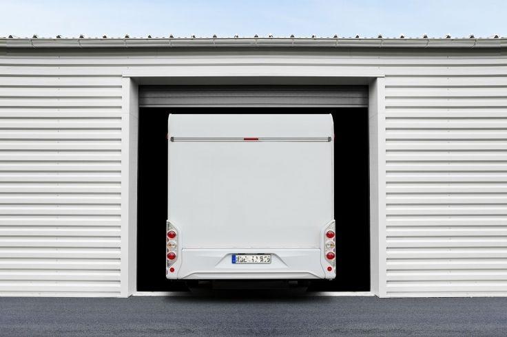 Heck eines wei&szlig;en Wohnmobils, teilweise in einer offenen Lagerbox mit geriffelter Metallwand; sichtbares Nummernschild