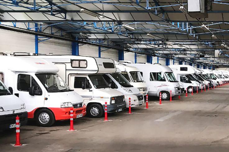 Reihe wei&szlig;er Wohnmobile in einer gro&szlig;en Halle, rote Absperrpfosten