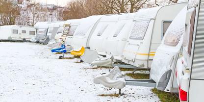 Reihe wei&szlig;er Wohnwagen auf schneebedecktem Boden; vor einigen Wagen kleine Boote auf Anh&auml;ngern; B&auml;ume und Geb&auml;ude im Hintergrund