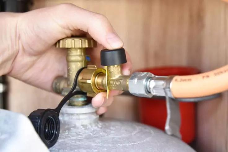 Hand h&auml;lt ein Messingventil an einer Metallarmatur, orangener Schlauch ist an einem Metallzylinder angeschlossen