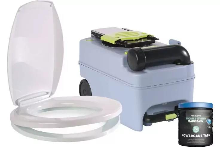 Offener wei&szlig;er Toilettensitz mit hochgeklapptem Deckel, daneben hellgraues rechteckiges Ger&auml;t mit schwarzem Griff, R&auml;dern und gelb-gr&uuml;nem Teil oben, vorn rechts kleine schwarze Dose mit blauem Deckel