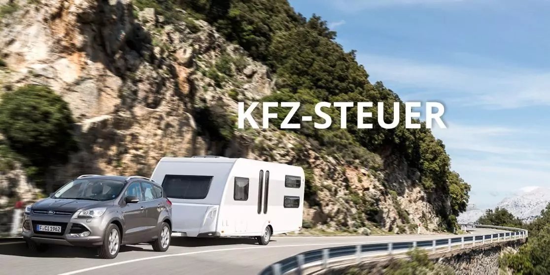 Auto mit wei&szlig;em Wohnwagen auf kurvenreicher K&uuml;stenstra&szlig;e neben Felswand und blauem Himmel, Schriftzug 'KFZ-STEUER'