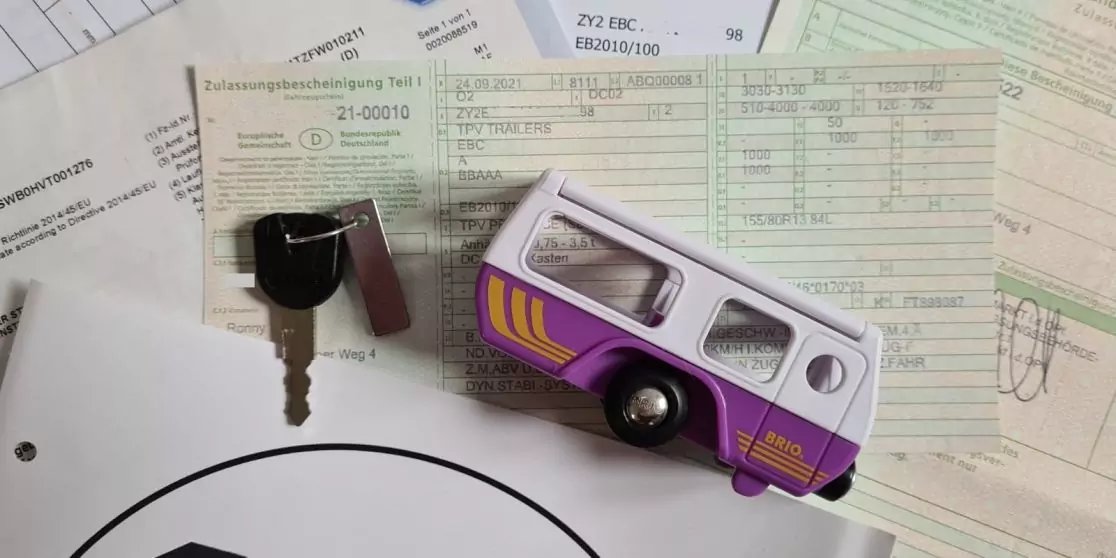 Mehrere bedruckte Formulare, darauf ein lila-wei&szlig;es Spielzeug-Van auf der Seite, ein Metallschl&uuml;ssel mit schwarzem Kunststoffkopf und ein Kugelschreiber