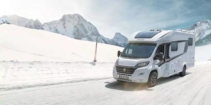 Wei&szlig;es Wohnmobil auf schneebedeckter Stra&szlig;e, im Hintergrund schneebedeckte Berge und blauer Himmel mit Wolken