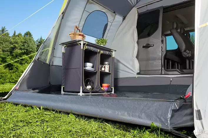 Offenes Vorzelt an einem Fahrzeug, kleiner Camping-Schrank mit Tassen, Sch&uuml;sseln und Pflanzen in T&ouml;pfen; Gras und B&auml;ume im Hintergrund