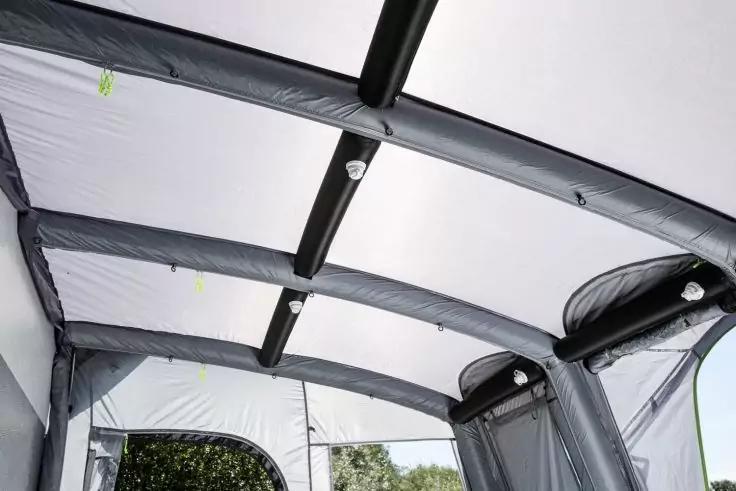 Innenansicht des Dachs einer aufblasbaren Zeltkonstruktion mit grauen, gebogenen Luftstreben, wei&szlig;er Bespannung und seitlichen Fenster&ouml;ffnungen, durch die B&auml;ume sichtbar sind