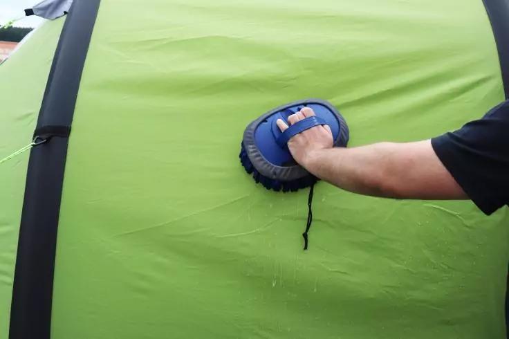 Unterarm in schwarzem Kurzarm hält blaues rundes Handgerät an eine grüne Stoffwand mit schwarzen vertikalen Streifen