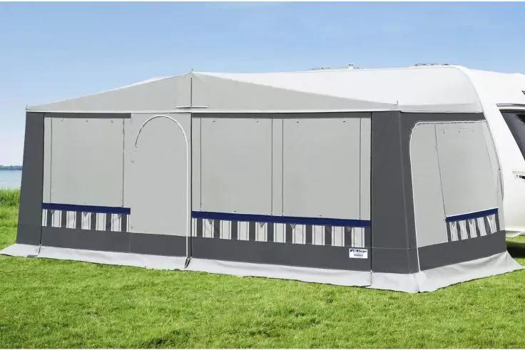 Graues Vorzelt an einem wei&szlig;en Wohnwagen auf gr&uuml;ner Wiese, im Hintergrund Wasser und blauer Himmel