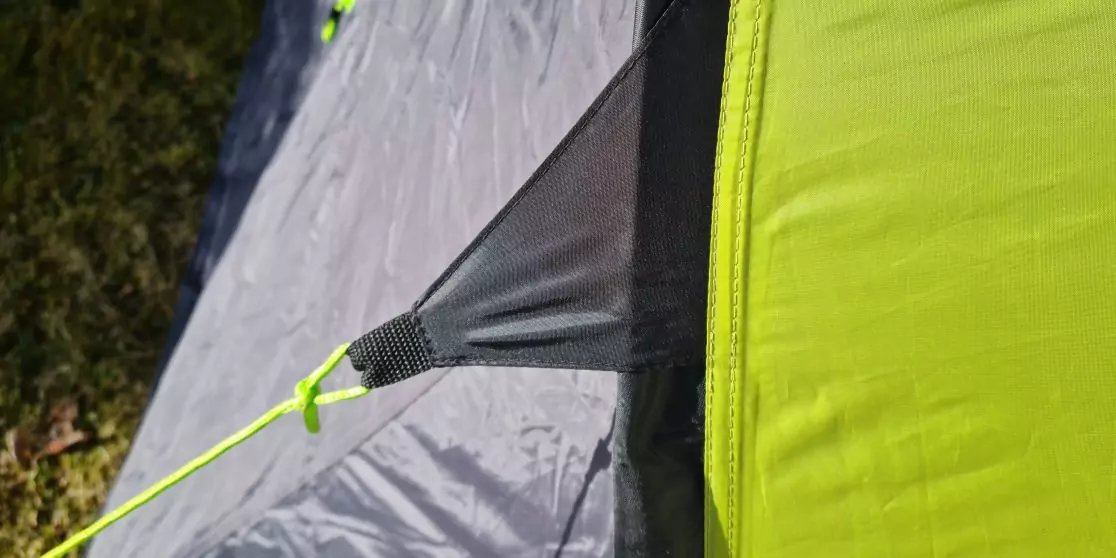 Primer plano de tela de tienda amarillo-verde en una esquina, suelo interior gris, lazo de fijaci&oacute;n negro y cuerda de sujeci&oacute;n amarillo ne&oacute;n