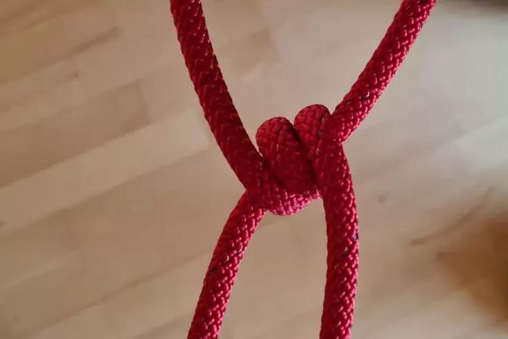 Rotes geflochtenes Seil mit Knoten vor hellem Holzfu&szlig;boden