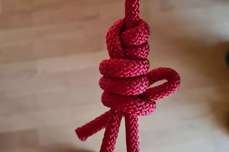 Rotes geflochtenes Seil mit mehreren Schlaufen und einem Knoten vor unscharfem Holzboden
