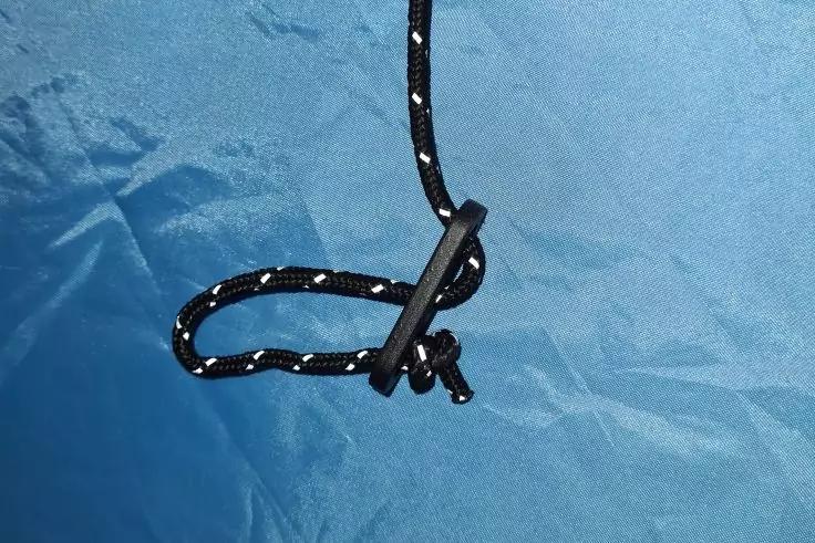 Schwarze Kordel mit wei&szlig;en Reflektorf&auml;den durch einen schwarzen Kunststoff-Kordelstopper gef&uuml;hrt, geknotetes Ende, auf blauem Stoff