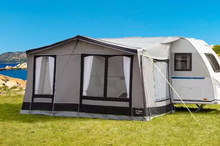 Wei&szlig;er Wohnwagen mit grauem Vorzelt auf einer Wiese, im Hintergrund Felsen, Meer und blauer Himmel