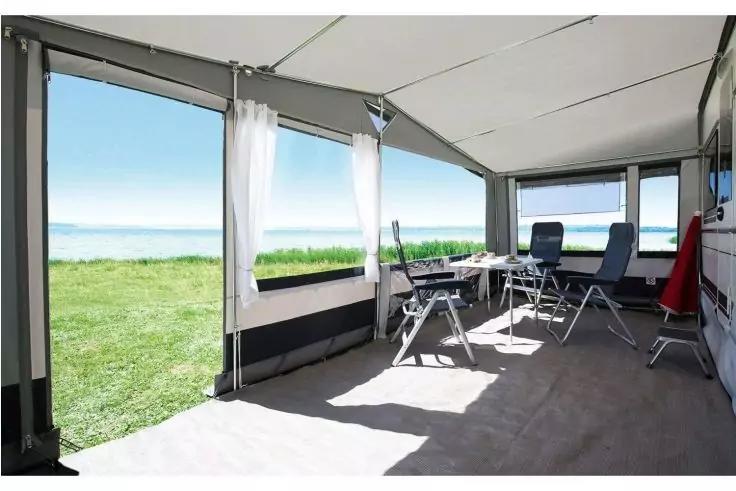 Innenraum eines ge&ouml;ffneten Campingvorzelts mit Tisch, Klappst&uuml;hlen, ge&ouml;ffneten Seitenw&auml;nden und Blick auf Rasen und Meer