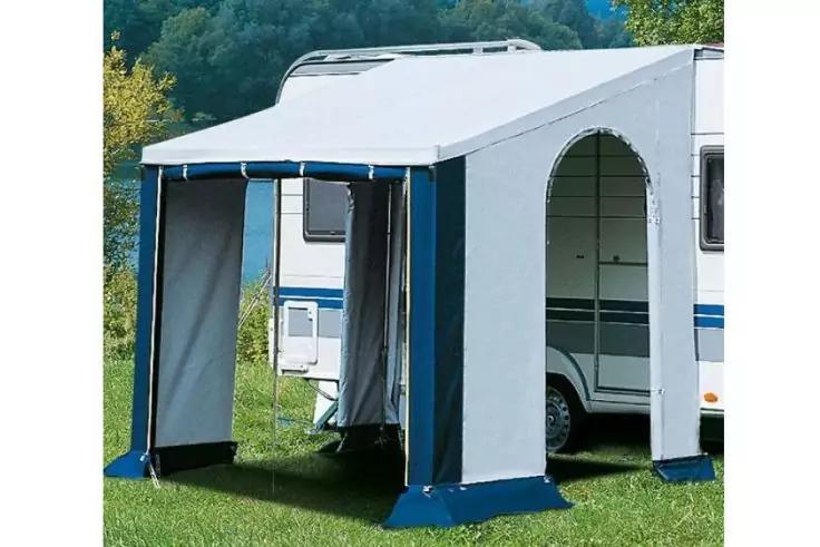 Wei&szlig;-graues Vorzelt mit blauem Saum an einem wei&szlig;en Wohnwagen auf einer gr&uuml;nen Wiese, B&auml;ume im Hintergrund