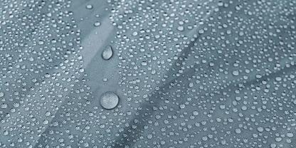 Nahaufnahme von Wassertropfen unterschiedlicher Gr&ouml;&szlig;e auf einer blaugrauen, leicht strukturierten Oberfl&auml;che