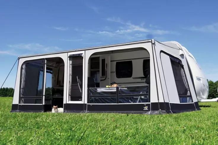 Großes hellgraues Vorzelt an weißem Wohnwagen auf grüner Wiese, sichtbare Fenster und offene Tür, blauer Himmel