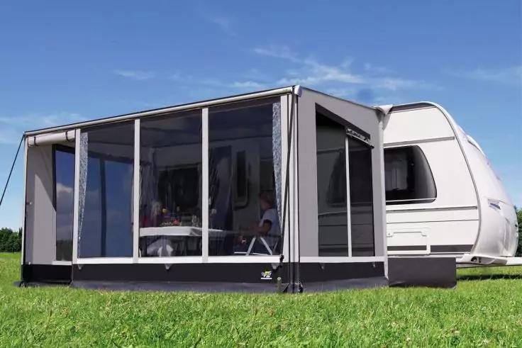 Wei&szlig;er Wohnwagen mit angebautem transparenten Vorzelt auf gr&uuml;nem Rasen unter blauem Himmel