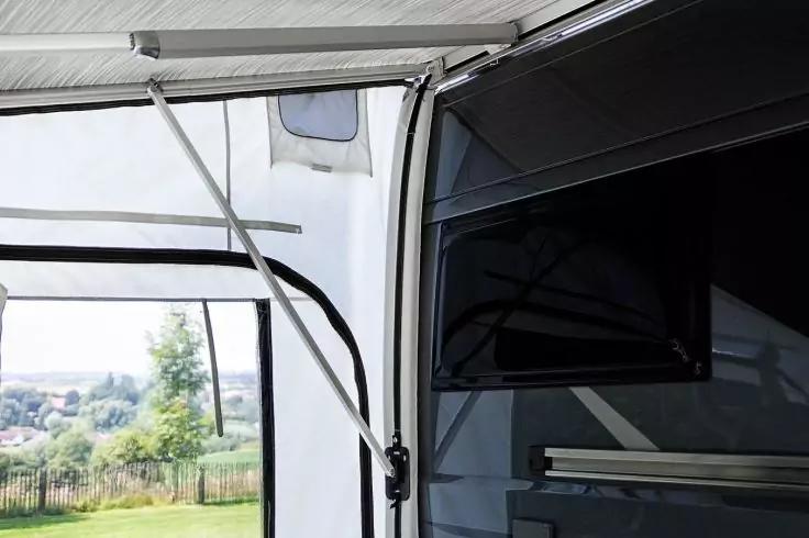 Wei&szlig;es Stoffdach mit Metallst&uuml;tzen, schwarzer Fernseher an dunkler Wand und durch ein offenes Seitenteil sichtbarer Rasen, B&auml;ume und H&auml;user im Hintergrund