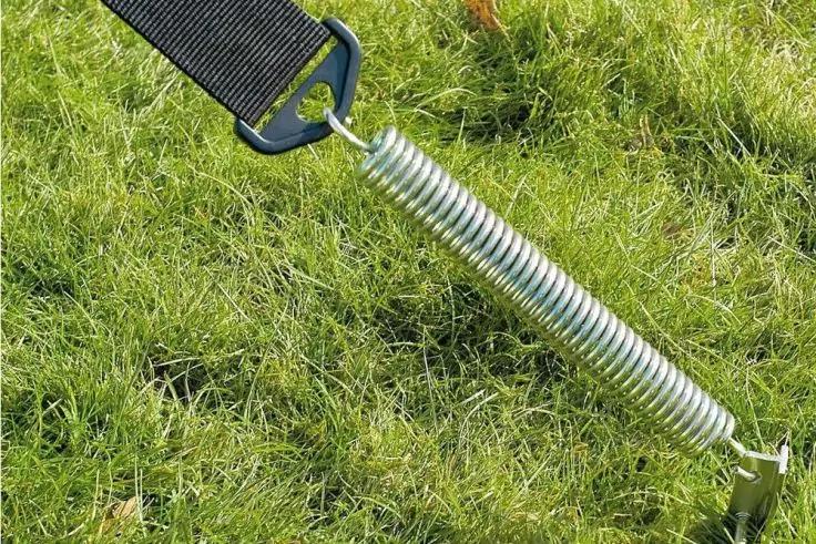Metallspiralfeder mit Haken, befestigt an einem schwarzen Gurt und einem Erdanker auf Gras